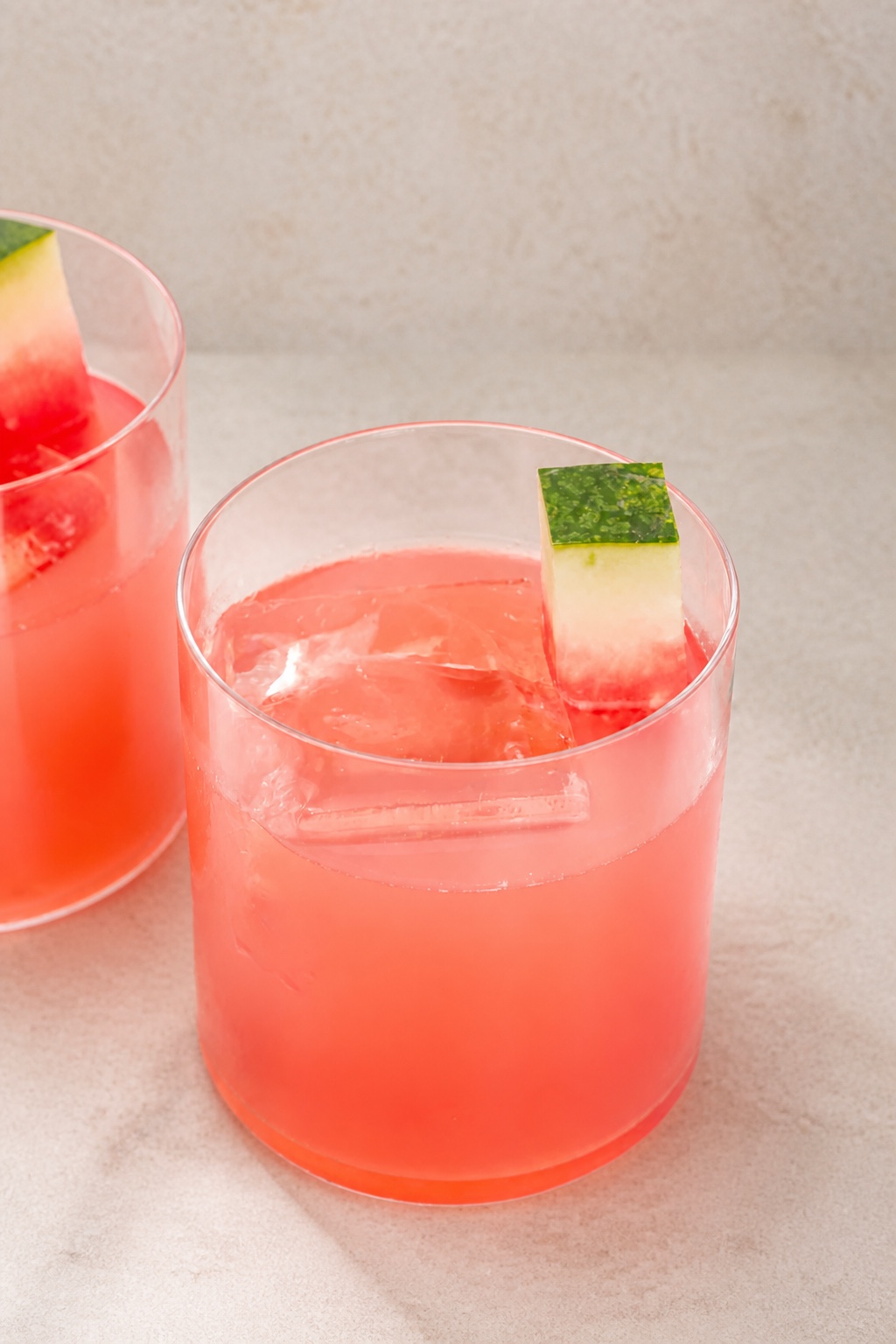 Two coral-pink After Training drinks served over ice on warm stone, each garnished with a watermelon-rind cube